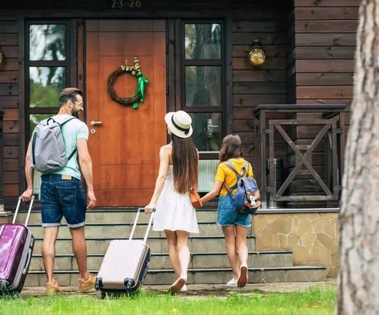 Familia con valijas llegando a la puerta de una cabaña de madera
